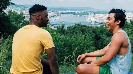 Two male Topdeck travelers laughing and joking with each other with a landscape view of Budapest in the background.