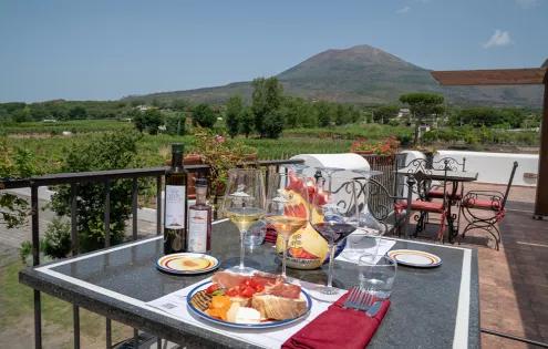 A spread of Italian delicacies adorn a table, with Mount Vesuvius featuring prominently in the background.