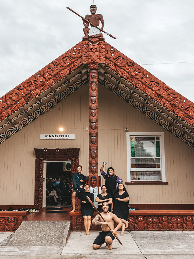Picture of a Maori native with a pole posing for the with a Topdeck tour group.